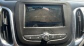 Infotainment screen showing rearview camera feed with parking guide lines in a parking lot in front of vehicles and buildings behind the car.