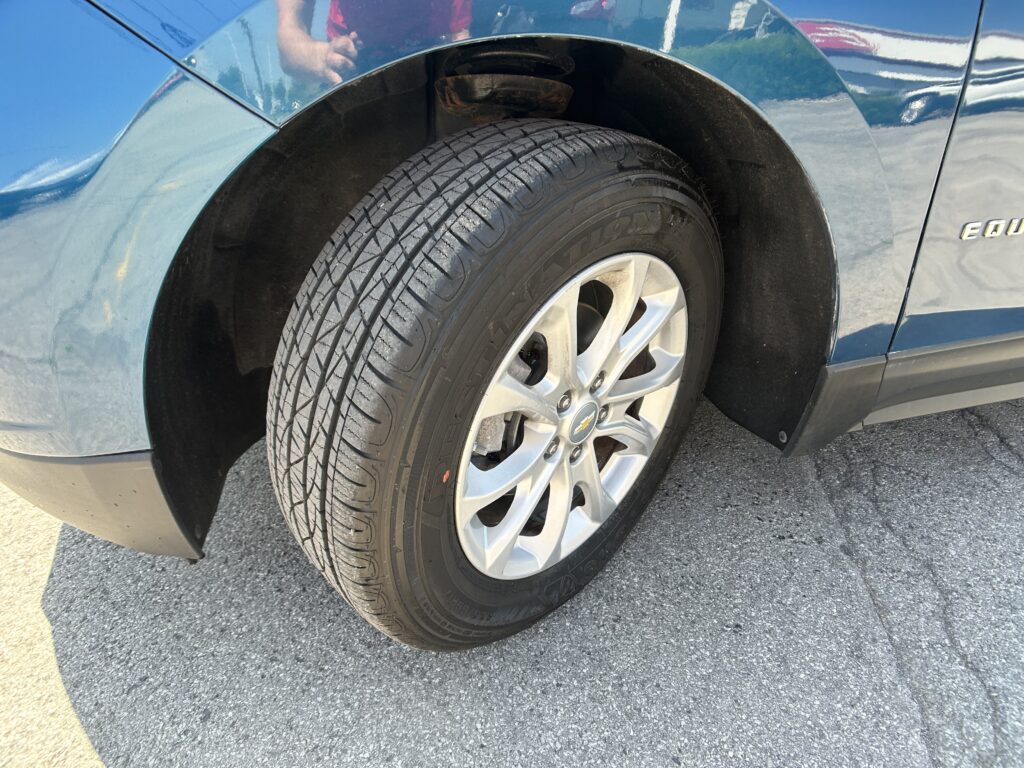 Close-up of a blue SUV front wheel and tire, showing wheel well and the Equinox badge on the side panel.