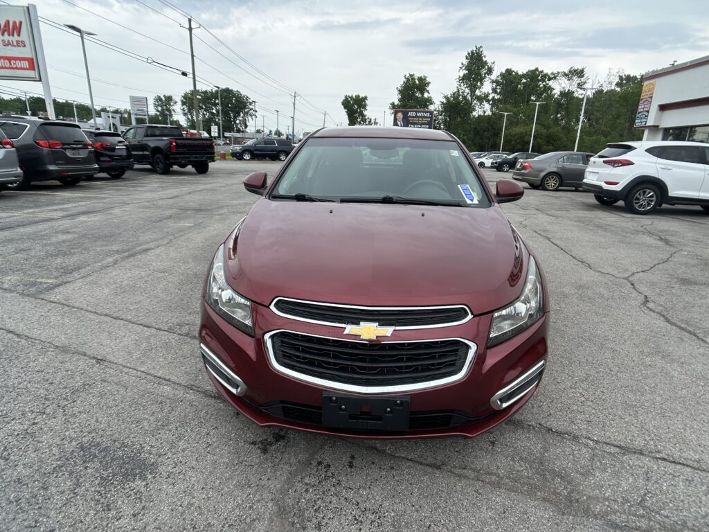 Front view of a maroon Chevrolet SUV in a dealership parking lot with other cars and a billboard in the background