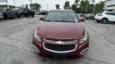 Front view of a maroon Chevrolet SUV in a dealership parking lot with other cars and a billboard in the background