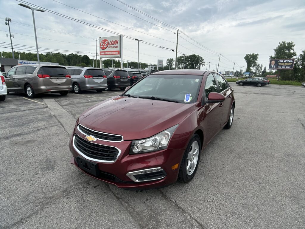 Maroon Chevrolet sedan in a dealership lot with white minivans parked behind and an EZ LOAN Auto Sales sign in the background.