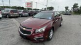 Maroon Chevrolet sedan in a dealership lot with white minivans parked behind and an EZ LOAN Auto Sales sign in the background.