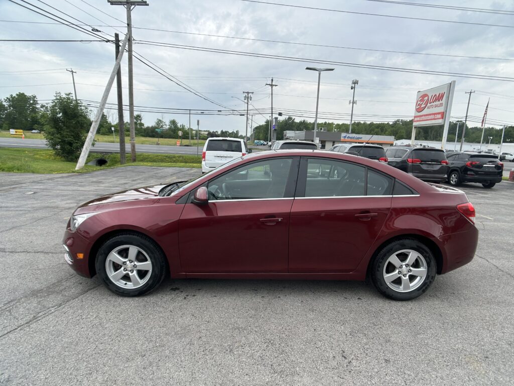 Red sedan parked in a lot with other cars and power lines overhead, near a dealership sign in the background.