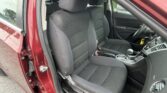 Open-car-door view of a black fabric front seat and passenger seat in a red SUV, steering wheel visible on the right side.