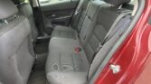 Back seat interior of a red car with black fabric seats, three headrests and belt buckles visible, door panel in view.