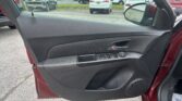 Inside view of a car door with window controls, looking out at a parking lot full of cars with a white SUV centered in the background.