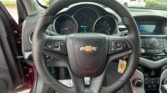 Driver's view of car dashboard: steering wheel in focus, gauge cluster, and center console with digital display showing speed 0, in a parking lot.