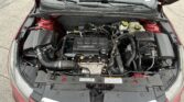 Engine bay of a red car with hood open, showing an Ecotec engine cover and various hoses and reservoirs.