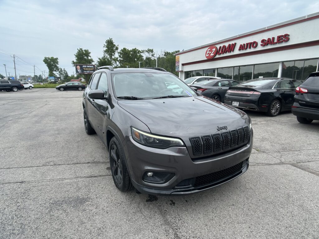 Gray Jeep SUV in the foreground at an auto dealership lot, with the EZ Loan Auto Sales sign and other cars in the background.