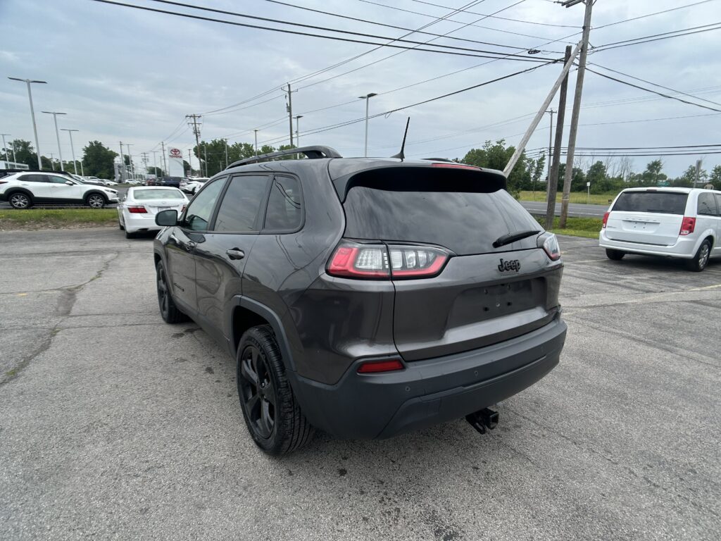Rear view of a gray Jeep SUV parked in a car dealership lot with other vehicles nearby and power lines overhead