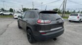 Rear view of a gray Jeep SUV parked in a car dealership lot with other vehicles nearby and power lines overhead