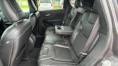 Back seat of a black leather SUV showing center armrest with cup holders and three seat belts while parked outside.