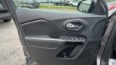 Open car door interior: black plastic door panel with window controls and silver door handle, parking lot visible outside.