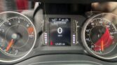 Close-up of a car dashboard: central display shows speedometer and mileage, with RPM gauge on left and speed gauge on right, car at rest.