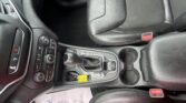 Interior of a car highlighting the center console, gear shifter, and cup holders with black leather seats and a red seatbelt buckle visible on the side