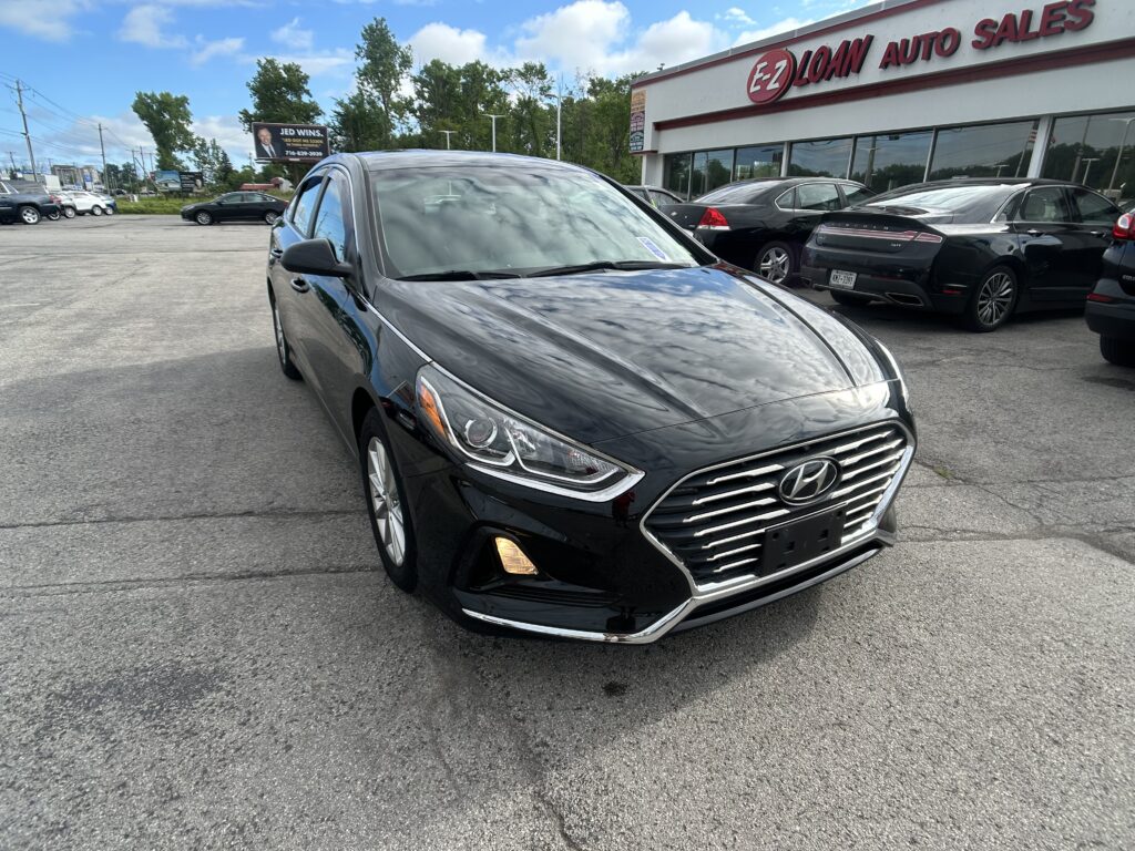Black Hyundai SUV parked diagonally in a car lot in front of an auto dealership with a red EZ LOAN AUTO SALES sign.