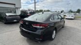 Black Hyundai Sonata in the foreground at a car dealership lot, with several other cars and a white showroom building on the left.