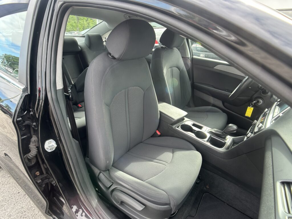 Front interior of a dark gray car with two front seats, center console, and steering wheel visible through the open driver's door.