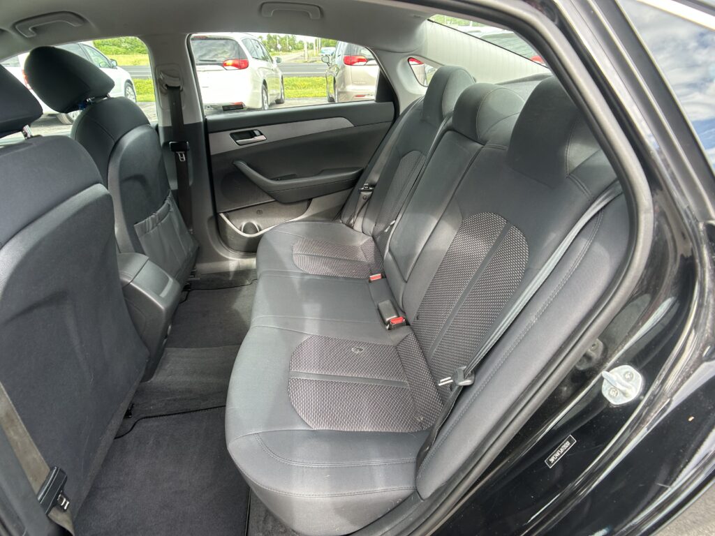 Rear passenger seats in a dark cloth car interior, view from open rear door, showing seat belts and door panel details
