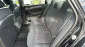 Rear passenger seats in a dark cloth car interior, view from open rear door, showing seat belts and door panel details