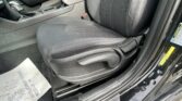 Front passenger seat and center console area of a car, with the gear shifter, seat belt buckle, and door jamb showing yellow warning labels nearby.