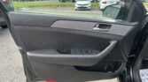 Interior of a car door with window controls, armrest, and side mirror visible, parking lot beyond.