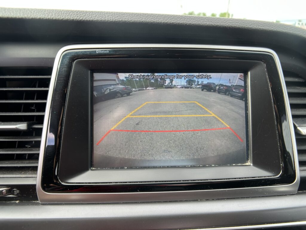 Rearview camera screen with parking guidelines and a street scene; text reads 'Check surroundings for your safety'.
