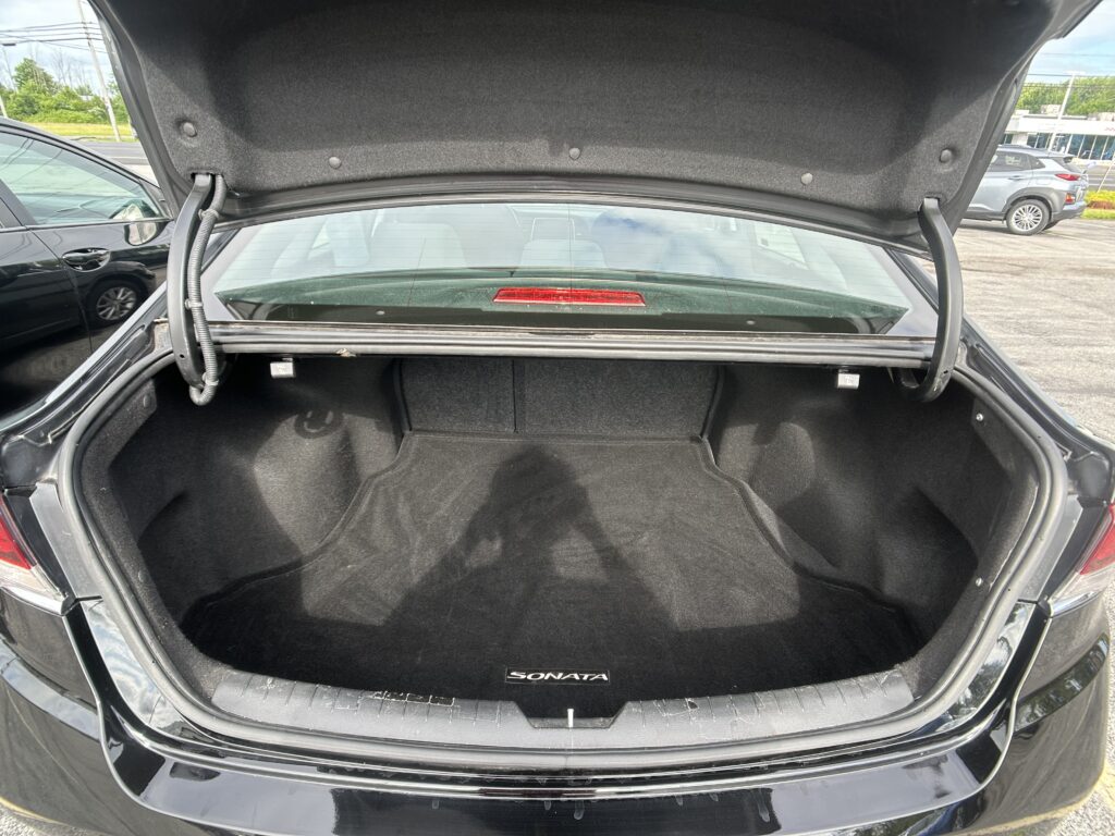 Open trunk of a black Hyundai Sonata, showing the empty cargo space and rear windshield view behind it.