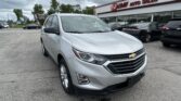 Silver Chevrolet SUV in the foreground at an auto dealership lot, EZ LOAN AUTO SALES visible on the building with other cars parked nearby under a cloudy sky.