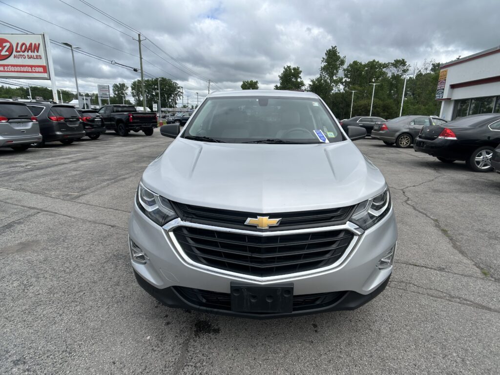 Front view of a silver Chevrolet SUV parked in a dealership lot, with other cars and an EZ Loan Auto Sales sign in the background.
