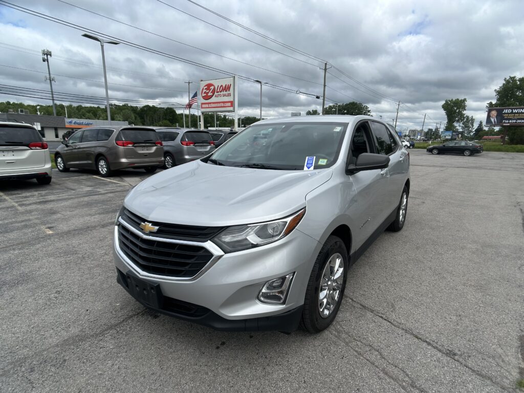 Silver Chevrolet SUV in foreground at a used car lot with multiple minivans parked behind; EZ Loan Auto Sales sign and cloudy sky overhead