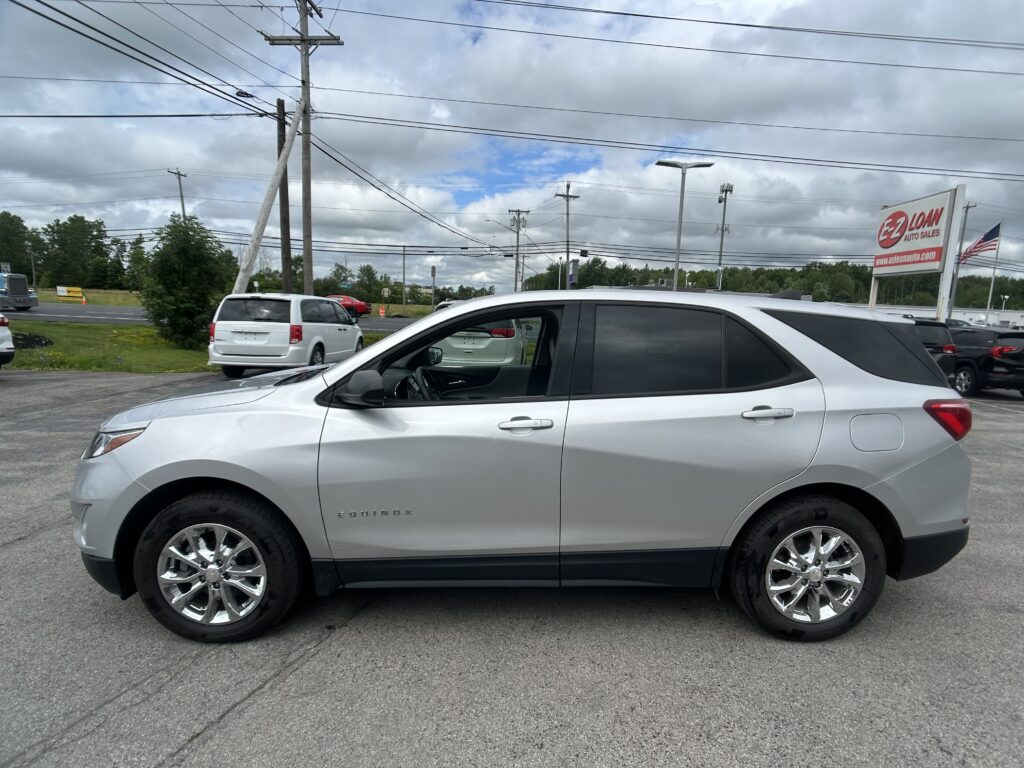 Silver Chevrolet Equinox in a parking lot, with power lines overhead and an EZ LOAN Auto Sales sign on the right and an American flag nearby.