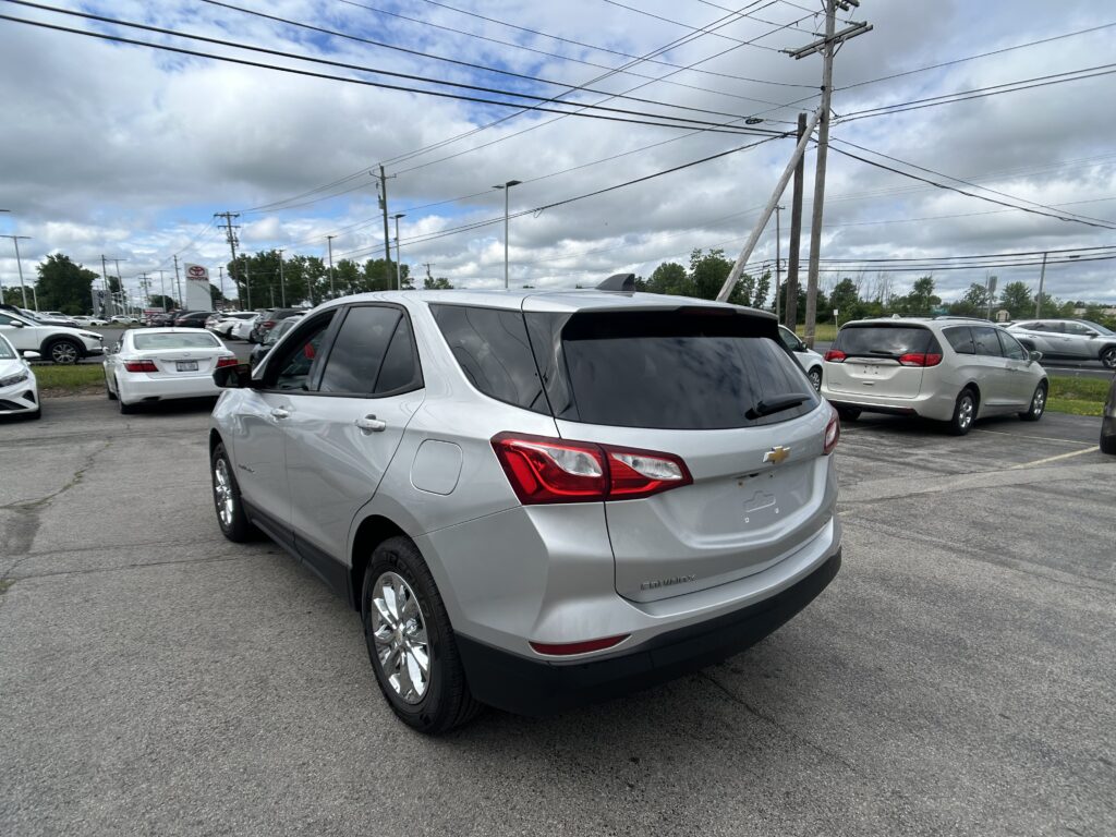 Silver SUV (Chevrolet Equinox) dominates foreground in a car dealership parking lot with many other cars and power lines overhead.
