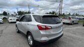 Silver SUV (Chevrolet Equinox) dominates foreground in a car dealership parking lot with many other cars and power lines overhead.