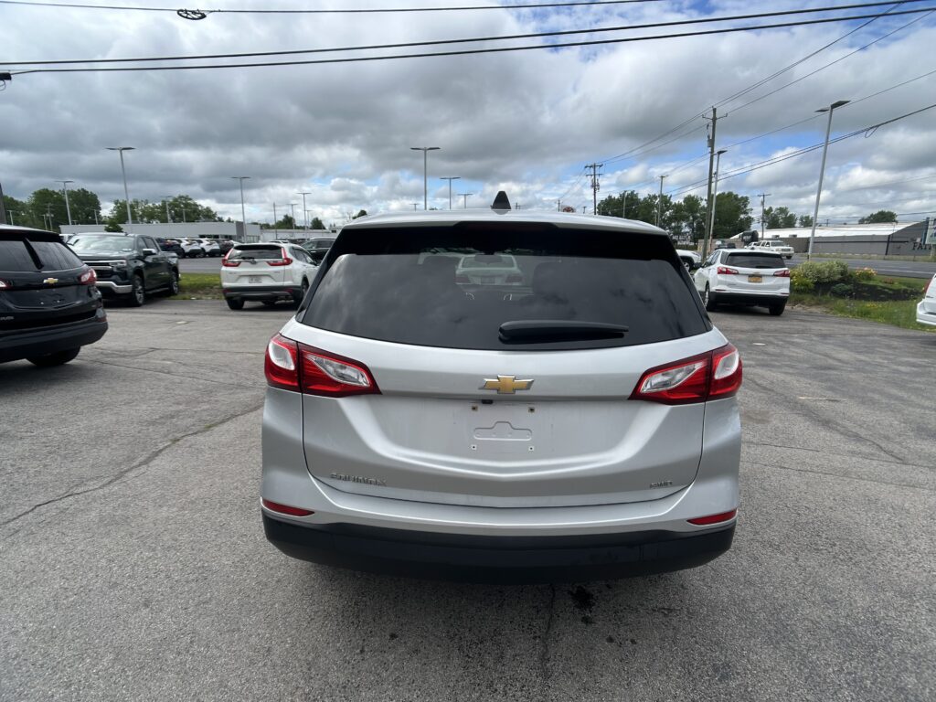 Rear of a silver Chevrolet Equinox parked in a lot, other cars around, cloudy sky above and power lines.