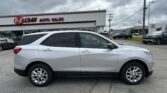 White Chevrolet Equinox parked in a dealership lot with E-Z Loan Auto Sales sign on a building in the background and a Toyota showroom across the street.