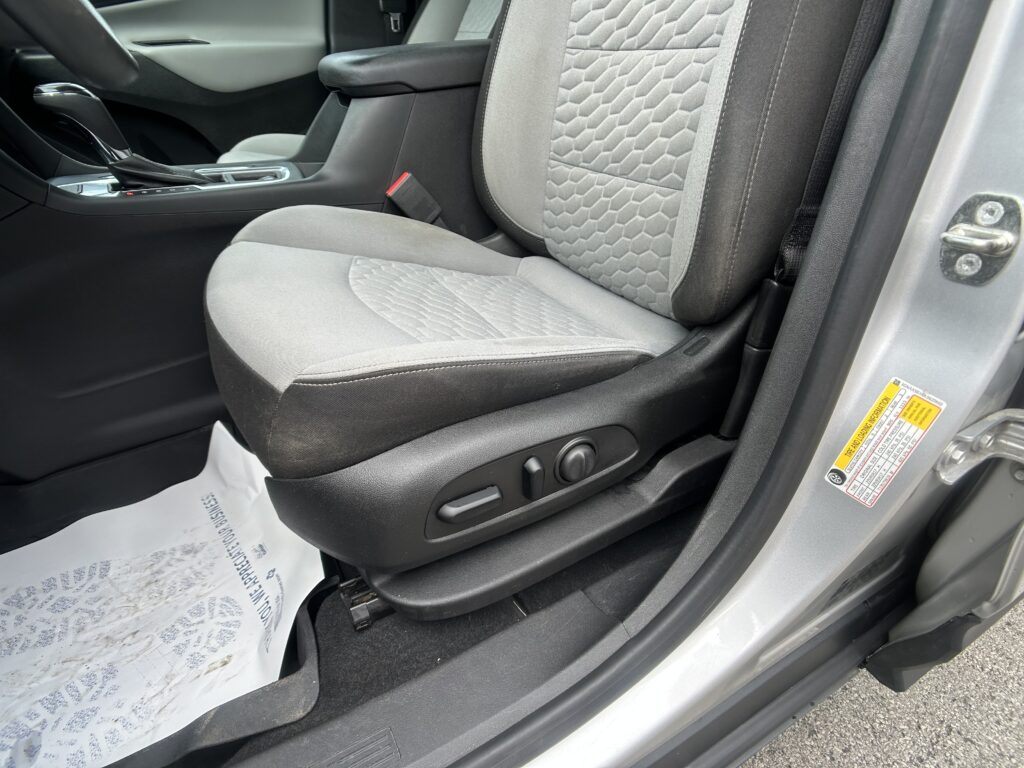 Front passenger seat and center console of a car interior, with seat belt buckle visible and floor mat underneath.