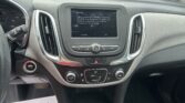 Car interior showing center infotainment screen with a driving warning; outside view shows a parking lot through the windshield.