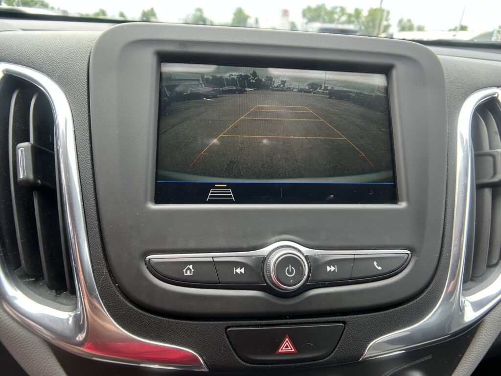 Back-up camera view on the dashboard screen showing yellow parking guide lines in a parking lot.