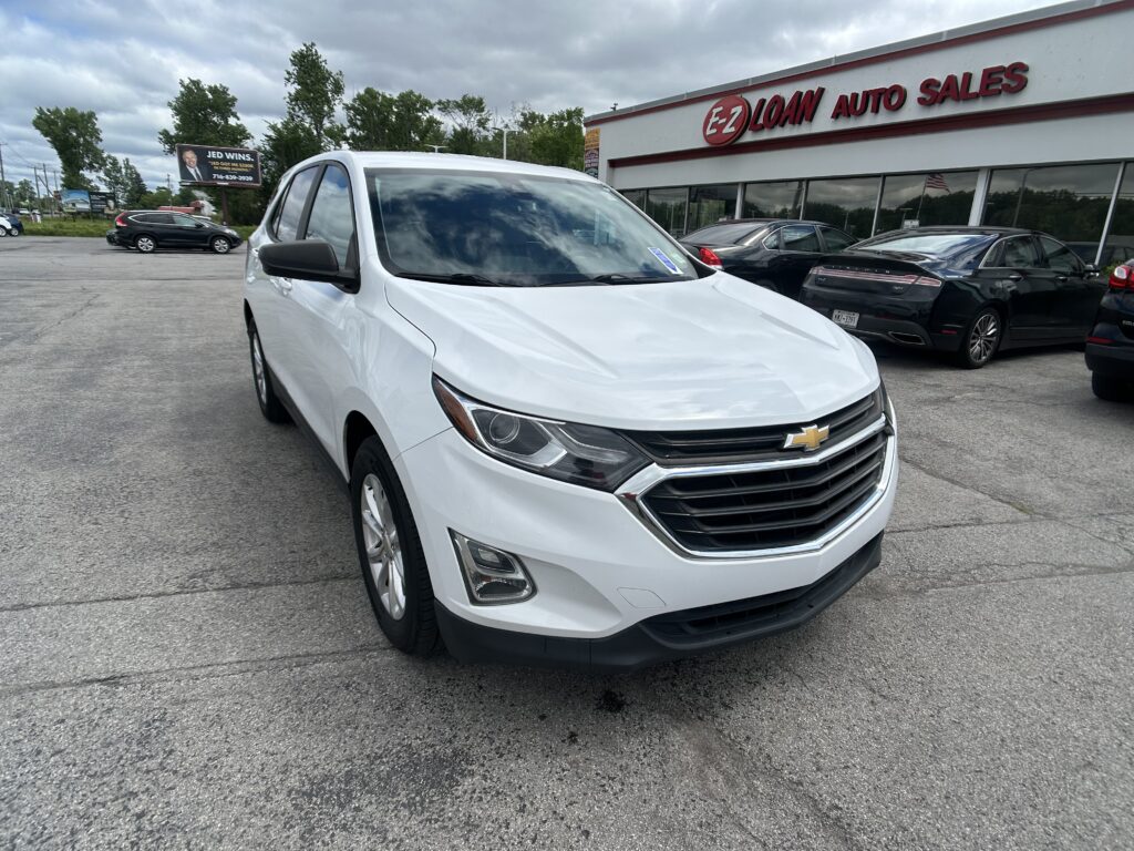 White Chevrolet SUV parked in front of EZ Loan Auto Sales with other cars and a showroom in the background, under a cloudy sky.