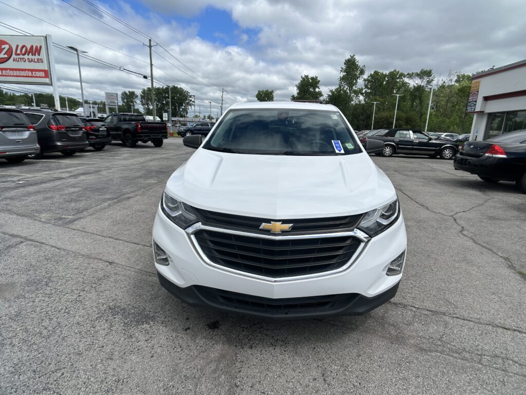 White Chevrolet SUV in a dealership lot, front view with other cars and a red EZ Loan Auto Sales sign in the background under a cloudy sky.