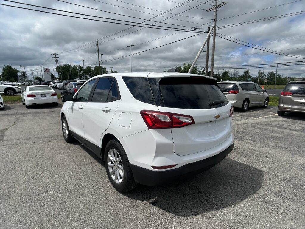 White SUV in a crowded parking lot with other cars and overcast sky above power lines.
