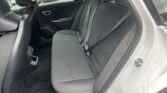 Gray fabric rear seat in a car with two headrests, shoulder belts, and a view of parked vehicles outside through the windows.