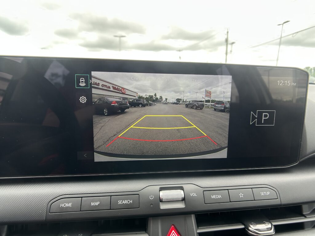 Rearview camera display showing parking guidelines (yellow, red, and green lines) over a car lot as the vehicle backs up.