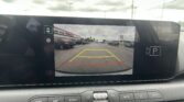 Rearview camera display showing parking guidelines (yellow, red, and green lines) over a car lot as the vehicle backs up.