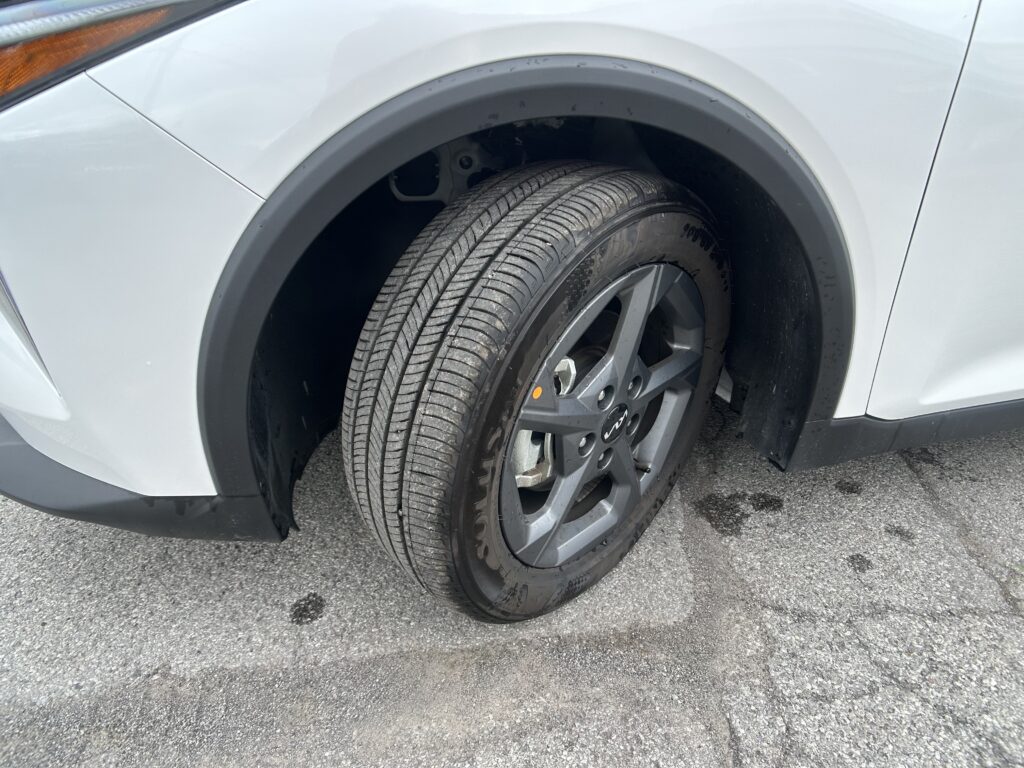 Close-up of a light-colored car’s front left wheel and tire in the wheel arch.
