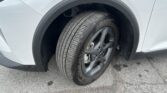 Close-up of a light-colored car’s front left wheel and tire in the wheel arch.