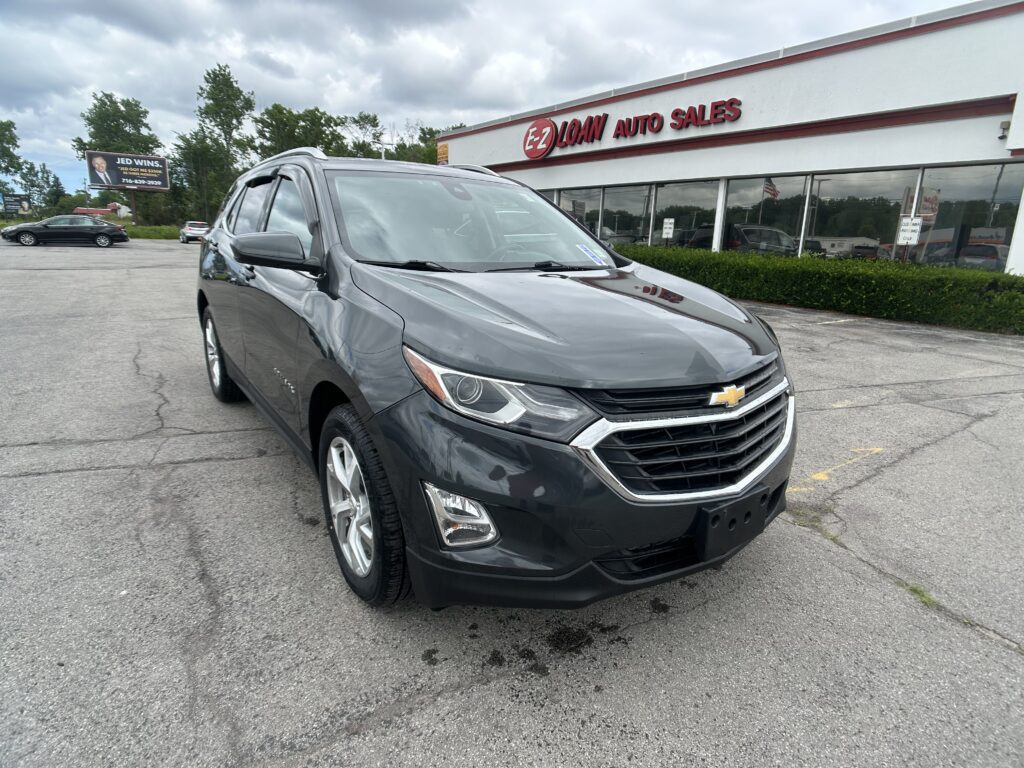 Gray Chevrolet SUV in a parking lot past an E-Z Loan Auto Sales storefront with a cloudy sky in the background