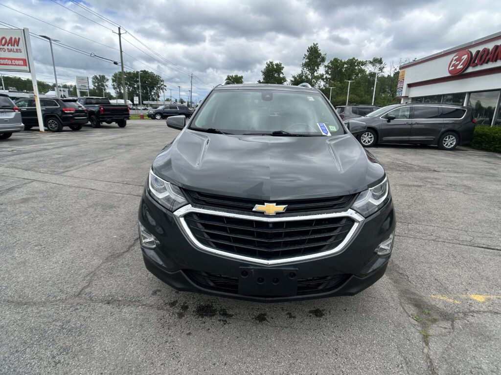 Front of a gray Chevrolet SUV in a parking lot near an EZ Loans dealership with other cars and cloudy sky in background