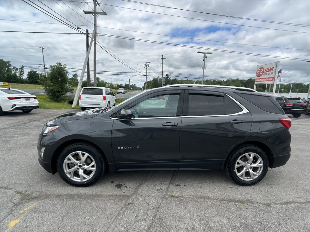 Gray Chevrolet Equinox parked in foreground at a car lot with power lines and a red EZ Loan Auto Sales sign in the distance, cloudy sky above 2024-07-07 edge of lot.
